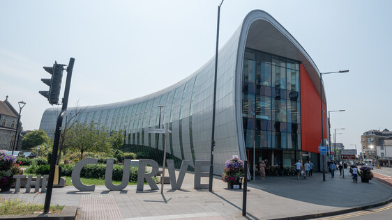 External shot of Curve venue, a horn shaped metallic and glass building with the word Curve in 3D metal letters at the front