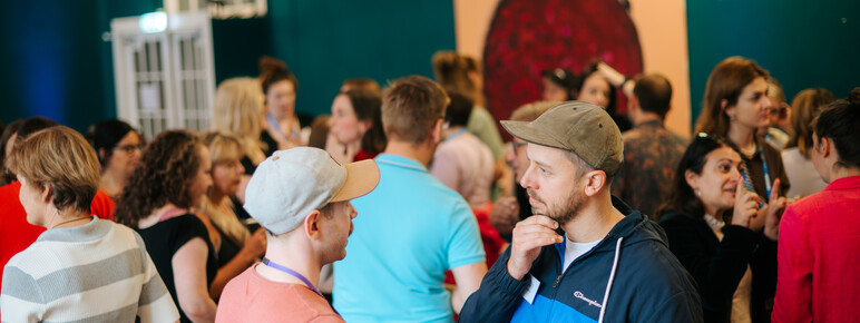 Crowd of artists and venue representatives in a bright room in focused discussions to one another.