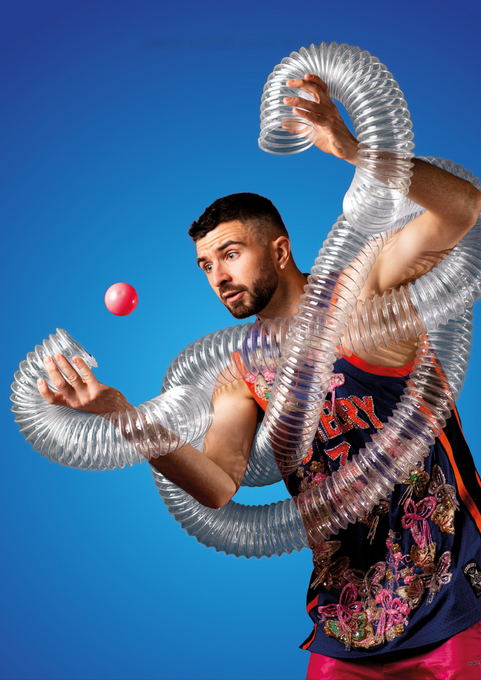 A man wrapped in a clear plastic tube gazes at a juggling ball aimed for the tube