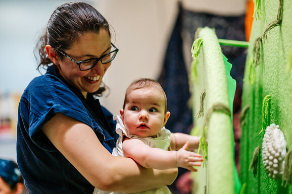 White woman with brown hair holding her baby up to the soft green set.