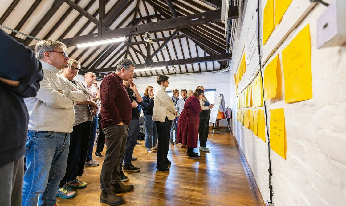 Group of people look at wall covered in large post it notes, house Network Day 2026