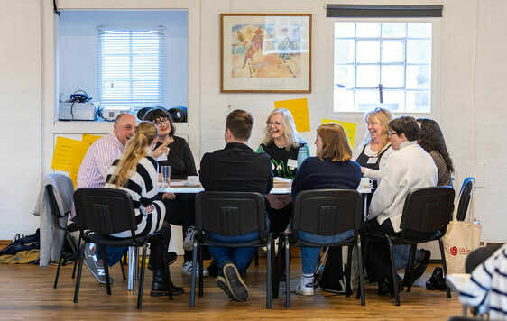 Group of nine people sat around a table chatting, house Network Day 2026