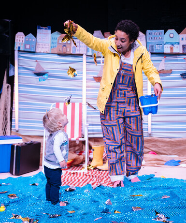 In bright lighting, the performer hangs some glittery fabric above a toddler
