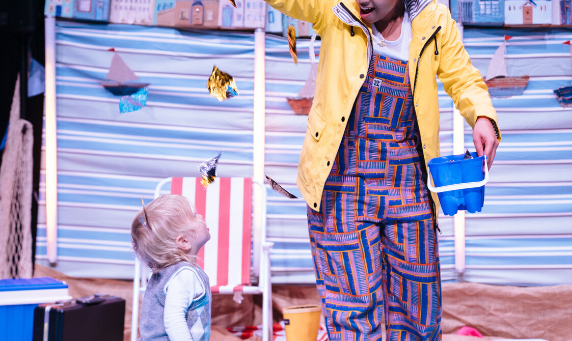 In bright lighting, the performer hangs some glittery fabric above a toddler