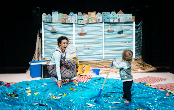 Performer is kneeled in front of a toddler who is facing away from the camera.