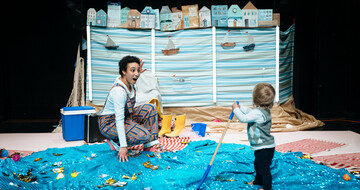 Performer is kneeled in front of a toddler who is facing away from the camera.
