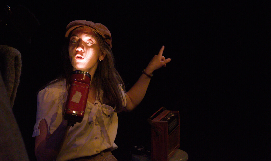 One performer holding a torch to illuminate their face whilst talking to the audience.