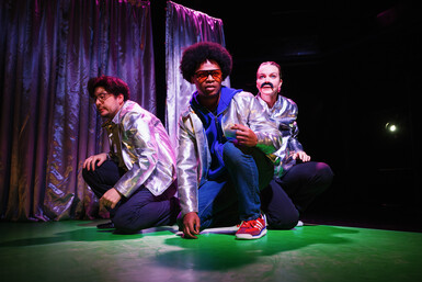 All three performers are crouching with silver jackets on.