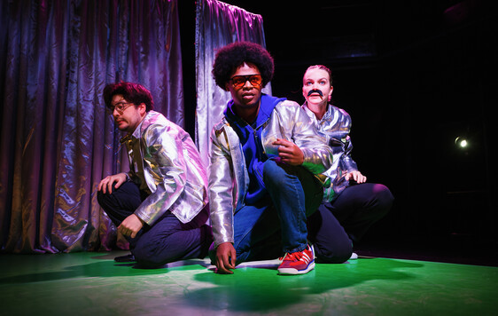 All three performers are crouching with silver jackets on.