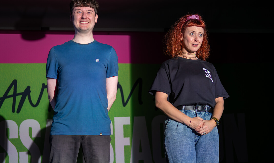 Both performers stand smiling intensely at the audience.