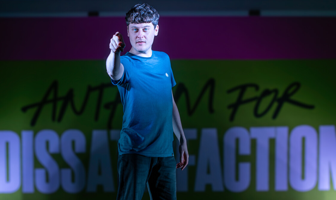 The actor playing Jamie stands centre-stage staring directly into the camera pointing.