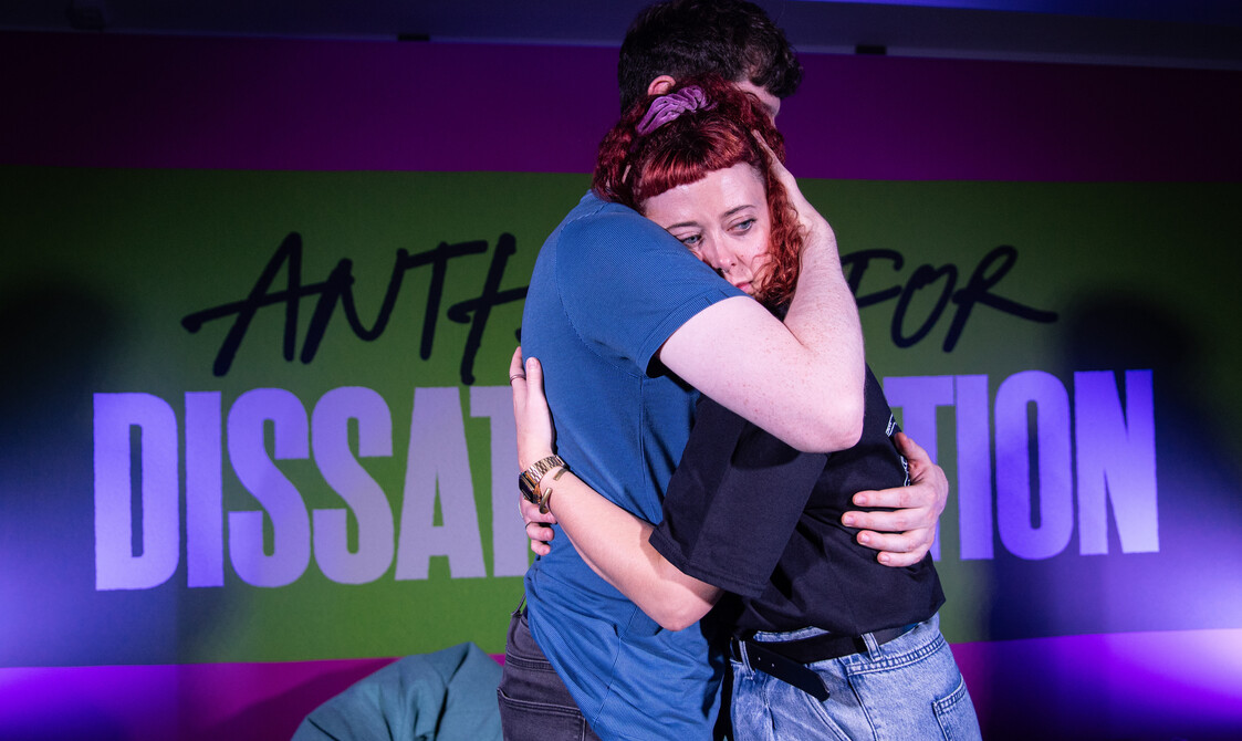 Two performers are hugging. Sarah is looking forlorn and concerned.