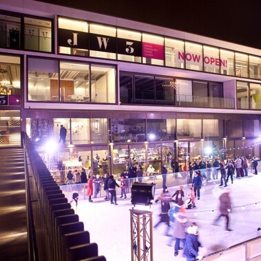 Glass fronted building JW3 theatre, with ice rink and blurred ice skaters lit up at night