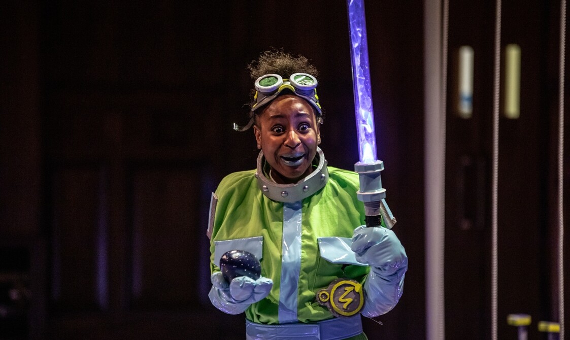 Woman wearing goggles on her forehead, a yellow cape holding a light sabre