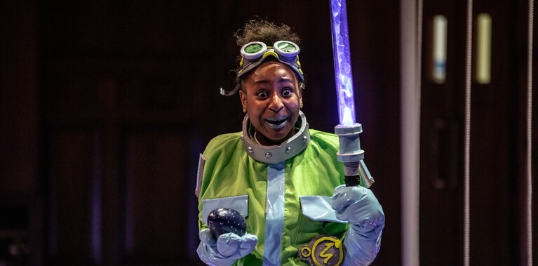Woman wearing goggles on her forehead, a yellow cape holding a light sabre