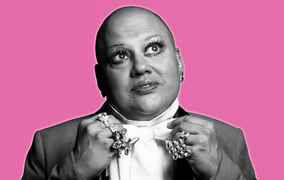 Black and white headshot of a man in white dress shirt and jacket, looking up. Wearing big rings on his hands.