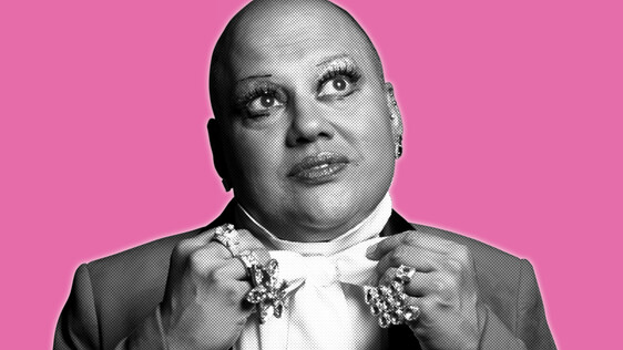 Black and white headshot of a man in white dress shirt and jacket, looking up. Wearing big rings on his hands.