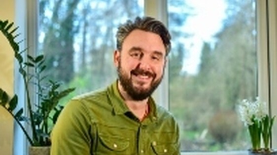 Headshot of George Perrin, a white man with facial hair wearing a green cord shirt