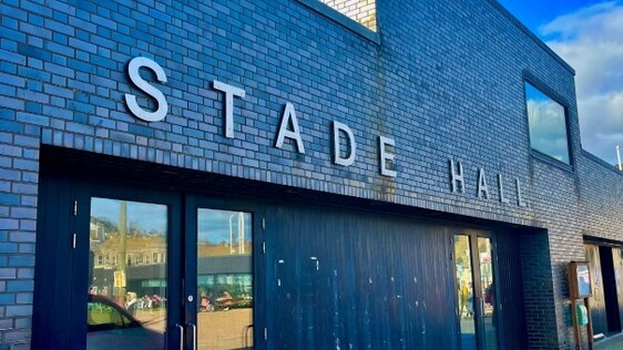 Outside brick and glass entrance of Stade Hall under a blue sky