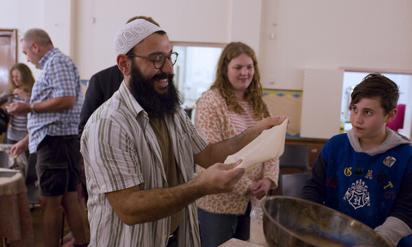 A man wearing a prayer cap with a long black beard reads baking instructions from a piece of paper to audience members